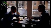 Young business people are eating food, sitting at table in cafe, two men talking, engaged in dialogue about project, enjoying delicious lunch by window in modern interior. Partners communicate opposite on wooden table. Concept: communication, day dining, partnership.